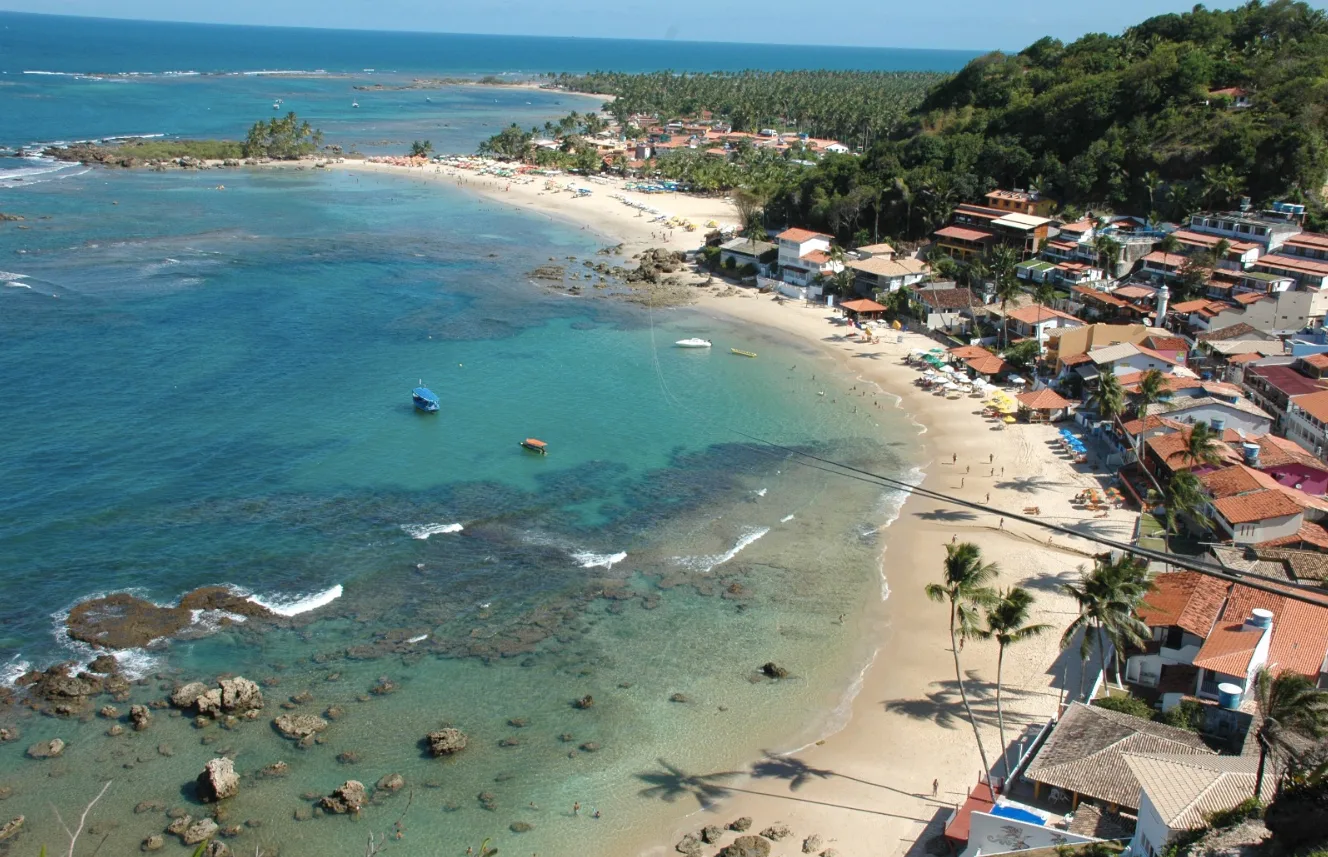 Vista aérea de uma praia de Boipeba, com mar turquesa, recifes e casario à beira-mar